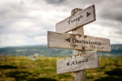 tough decisions ahead text quote written in wooden signpost outdoors in nature. Moody theme feeling.