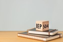 IEP Individual Education Plan Symbol. Section 504 program, text on a natural wooden block placed on school notebooks.